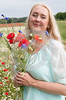 beautiful middle-aged blonde woman stands among a flowering field of poppies