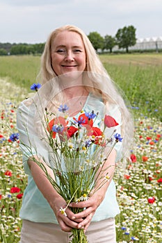 beautiful middle-aged blonde woman stands among a flowering field of poppies