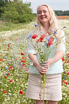 beautiful middle-aged blonde woman stands among a flowering field of poppies