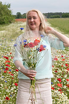 beautiful middle-aged blonde woman stands among a flowering field of poppies