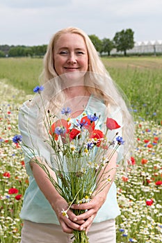 beautiful middle-aged blonde woman stands among a flowering field of poppies