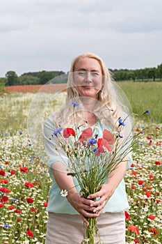 beautiful middle-aged blonde woman stands among a flowering field of poppies