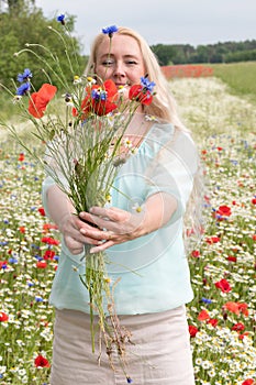 beautiful middle-aged blonde woman stands among a flowering field of poppies