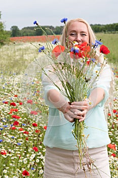 beautiful middle-aged blonde woman stands among a flowering field of poppies