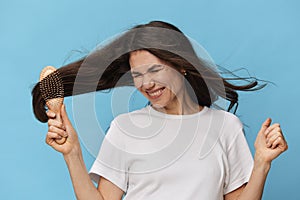beautiful, middle-aged brunette combing her long beautiful hair with a wooden comb and rejoicing loudly raising her hand