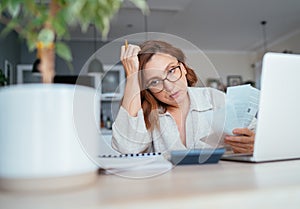 Beautiful middle-aged pensive woman in glasses with monthly bills thinking about family home budget. Small business, home finances