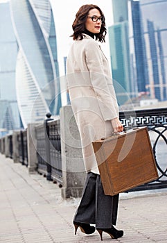 Beautiful middle-aged woman in a bright coat and a wooden case on a city background
