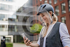 Beautiful middle-aged woman commuting through the city by bike, holding smartphone. Female city commuter traveling from