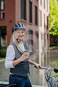 Beautiful middle-aged woman commuting through the city, buying, drinking coffe in front of office. Female city commuter