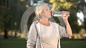 Beautiful middle aged woman drinking water after finishing her morning workout