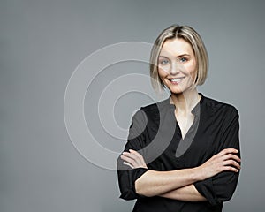 Beautiful middle-aged woman on a gray background in a black blouse smiling.