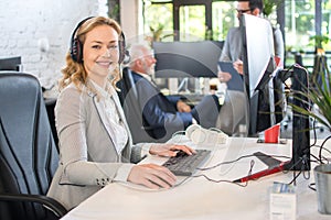 Beautiful middle aged woman with headphones working on computer in office