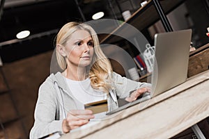 beautiful middle aged woman holding credit card and using laptop