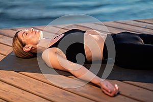 Beautiful middle aged woman lying in corpse pose while meditating outdoors