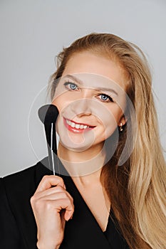 Beautiful middle aged woman makeup waving one makeup brush, winking at the camera and smiling. Blond hair and a black