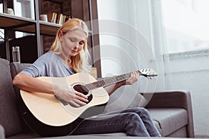 beautiful middle aged woman playing guitar while sitting on sofa