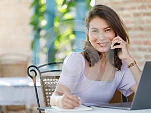 The beautiful middle-aged woman sitting in food shop and working with a laptop notebook computer and talking on the phone. Work