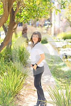 Beautiful middle aged woman smiling friendly and looking in camera in beautiful nature background.