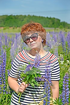 A beautiful middle-aged woman in sunglasses stands with a bouquet of blooming lupines in her hand
