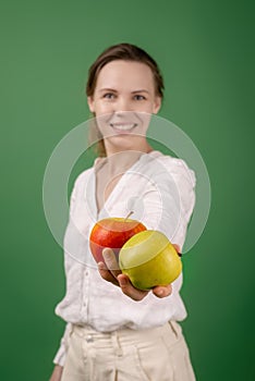 Beautiful middle-aged woman in a white shirt with apples on a green background. The concept of diet, healthy food, vegetarianism