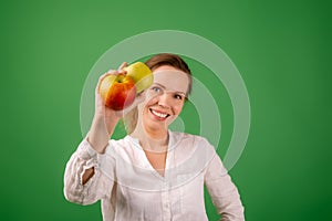 A beautiful middle-aged woman in a white shirt shows apples on a green background. The concept of diet, healthy food,