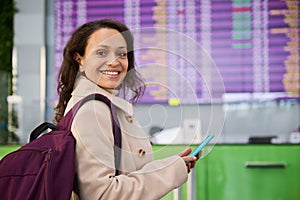 Beautiful Middle Eastern woman with backpack using mobile phone, browsing websites, making hotel reservations, smiling toothy