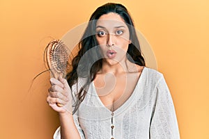 Beautiful middle eastern woman holding comb loosing hair scared and amazed with open mouth for surprise, disbelief face