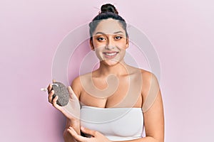Beautiful middle eastern woman holding pumice stone looking positive and happy standing and smiling with a confident smile showing