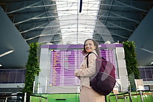 Beautiful Middle Eastern woman traveler with backpack smiling toothy smile looking over shoulder while standing in front of flight