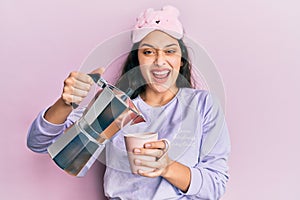 Beautiful middle eastern woman wearing sleep mask and pyjama drinking coffee celebrating crazy and amazed for success with open