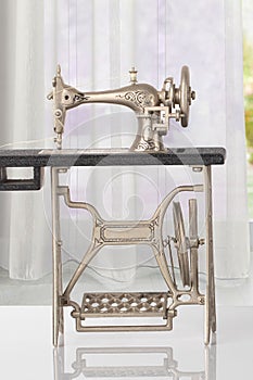 Beautiful miniature model of a vintage sewing machine on bright table over abstract bright curtain background. Advertisement for