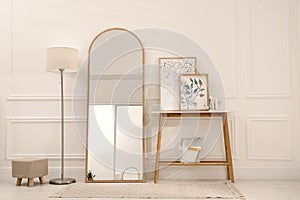 Beautiful mirror, console table and lamp near white wall indoors. Interior design