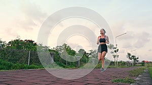 A beautiful mixed-race athlete in a sports top, shorts and sneakers is jogging along a red brick road. A girl runs in