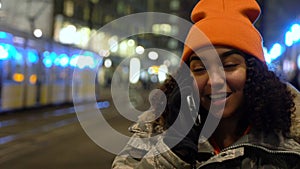 Beautiful mixed race female teenager girl young woman talking at night on cell phone at night with trams by Alexanderplatz Station