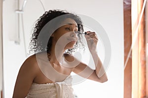 Beautiful mixed race woman looking in mirror applying mascara