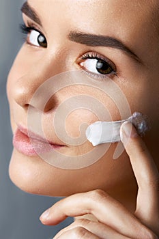 Beautiful model applying cosmetic cream treatment on her face. Close-up young beautiful face of girl applying moisturize cream