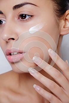 Beautiful model applying cosmetic cream treatment on her face white