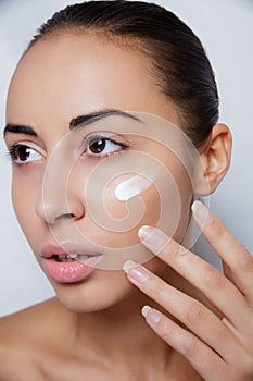 Beautiful model applying cosmetic cream treatment on her face white