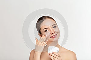 Beautiful model applying cosmetic cream treatment on her face on white background.