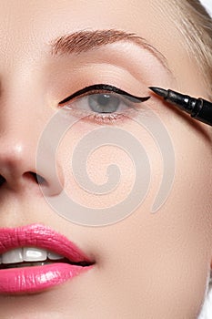 Beautiful model applying eyeliner close-up on eye. Make-up