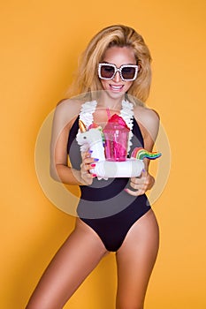 Beautiful model in a bikini and sunglasses, holding a drink and an inflatable pink flamingo.