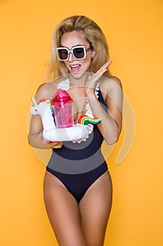 Beautiful model in a bikini and sunglasses, holding a drink and an inflatable unicorn.