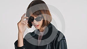 Beautiful model with bob hair and red lips in sunglasses looking in camera over white background