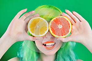 Beautiful model girl with colorful hairstyle takes red and yellow juice on green background
