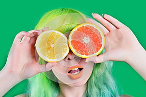 Beautiful model girl with colorful hairstyle takes red and yellow juice on green background