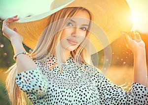 Beautiful model girl posing on a field, enjoying nature outdoors in wide brimmed straw hat. Beauty blonde young woman photo