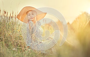 Beautiful model girl posing on a field, enjoying nature outdoors in wide brimmed straw hat