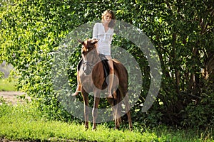 Beautiful model girl rides with horse in woods glade at sunset