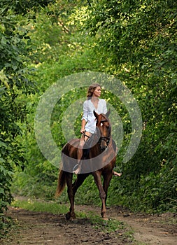 Beautiful model girl rides with horse in woods road in evening down