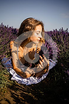 Beautiful model holding a bouquet of fresh lavenders relaxing in the spring or summer lavender field under the rays of the sun.